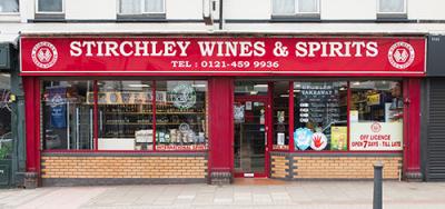 Stirchley Wines & Spirits storefront displays "Stirchley Wines & Spirits TEL: 0121-459 9936" with shop windows showcasing bottles and various advertisements. A sidewalk lies in front of the red and brick facade.