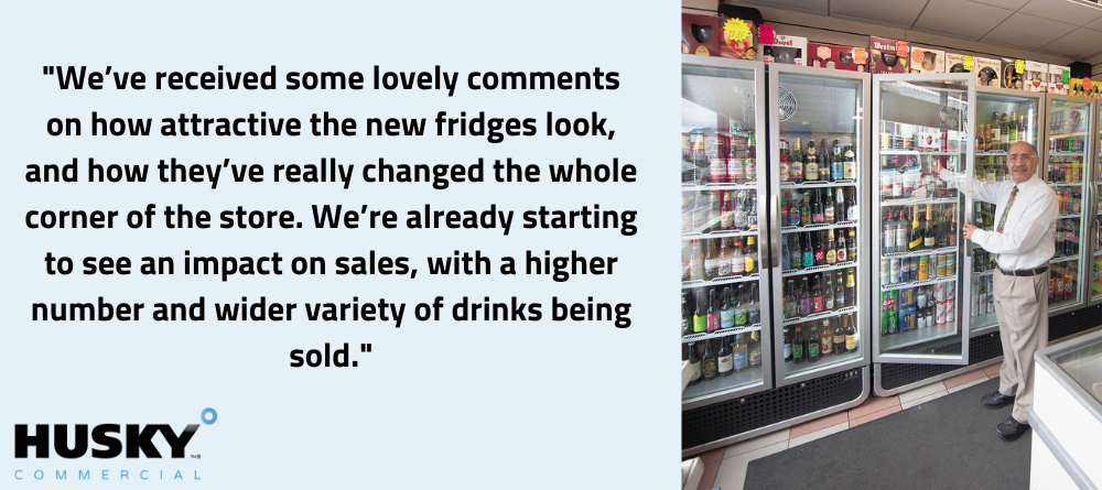 Large refrigerator units displaying drinks. An employee in white shirt and tie inspects the stocked shelves in a bright, modern store.