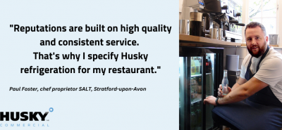 A man in a kitchen holds a bottled drink, kneeling next to a refrigerated cabinet. Text: "Reputations are built on high quality and consistent service. That's why I specify Husky refrigeration for my restaurant."