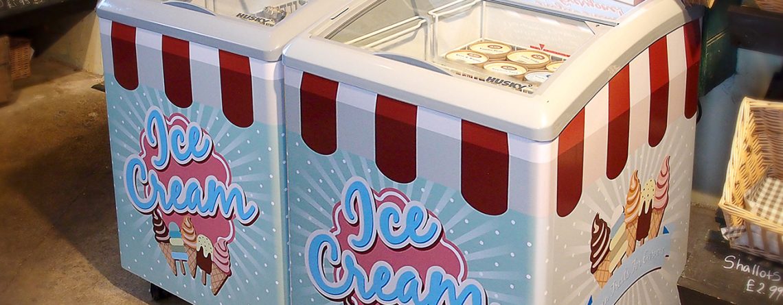 Large ice cream freezers, adorned with "Ice Cream" and "Frozen Treats For Everyone!" signs, sit side by side in a store selling various food items, including fresh produce and baked goods.