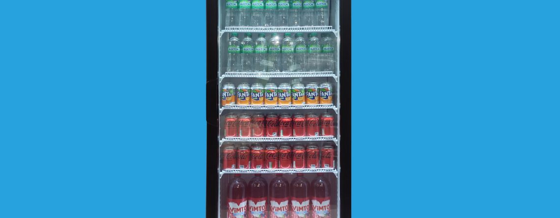 A black, illuminated beverage cooler containing multiple rows of assorted drink cans is centered against a solid bright blue background.