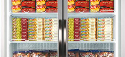 Frozen food items are displayed inside a commercial refrigerator with two glass doors; several shelves are stocked with pizzas, potato chips, and other packaged goods. Brands visible include "Ristorante," "McCain," "Aunt Bessie's," and "Birds Eye."