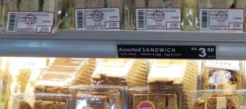Packaged sandwiches are displayed on refrigerated shelves, labeled "Shitake Chicken," "Mushroom," and "Egg." The bottom shelf has a sign reading "Assorted SANDWICH RM 3.50 each," with some packs labeled "NEW!"
