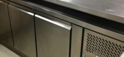 Stainless steel commercial refrigerator closed, placed in a kitchen environment with multiple storage doors and a vented side panel within a clean, sterile setting. No text present.