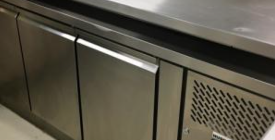 Stainless steel commercial refrigerator closed, placed in a kitchen environment with multiple storage doors and a vented side panel within a clean, sterile setting. No text present.
