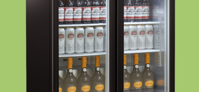 A refrigerated display case contains stacked Budweiser bottles, Stella Artois cans, and La Gioiosa orange-capped bottles, organized on three shelves in a retail environment.