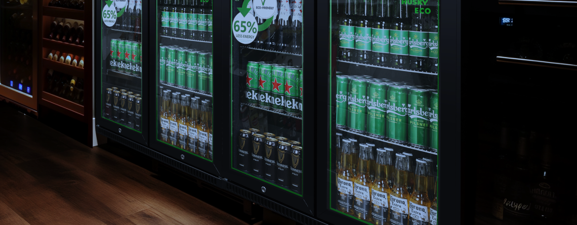 A sleek Husky Eco back bar fridge with glass doors, stocked with beer and beverages, featuring an energy-saving 65% less energy label. Ideal for bars and pubs looking for eco-friendly refrigeration solutions.