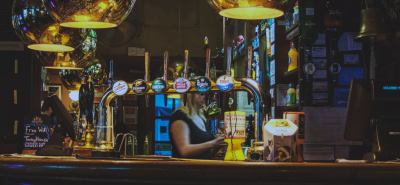 A classic British pub bar with beer taps, warm lighting, and a bartender serving customers, creating an inviting atmosphere for socialising and enjoying draft beers.