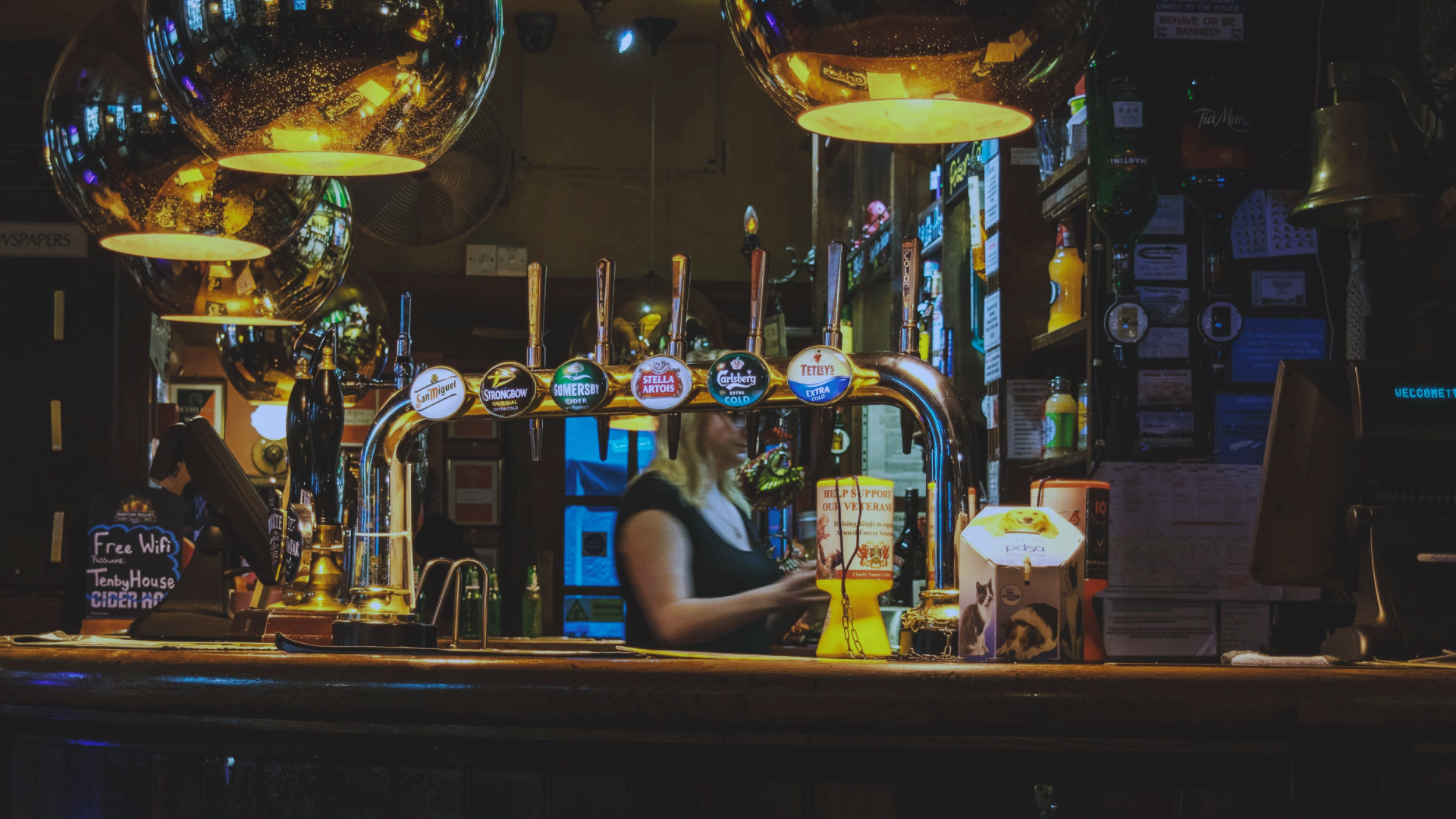 A classic British pub bar with beer taps, warm lighting, and a bartender serving customers, creating an inviting atmosphere for socialising and enjoying draft beers.