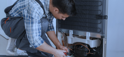 A skilled engineer kneeling and repairing a commercial fridge, performing routine maintenance to ensure optimal cooling performance and energy efficiency.