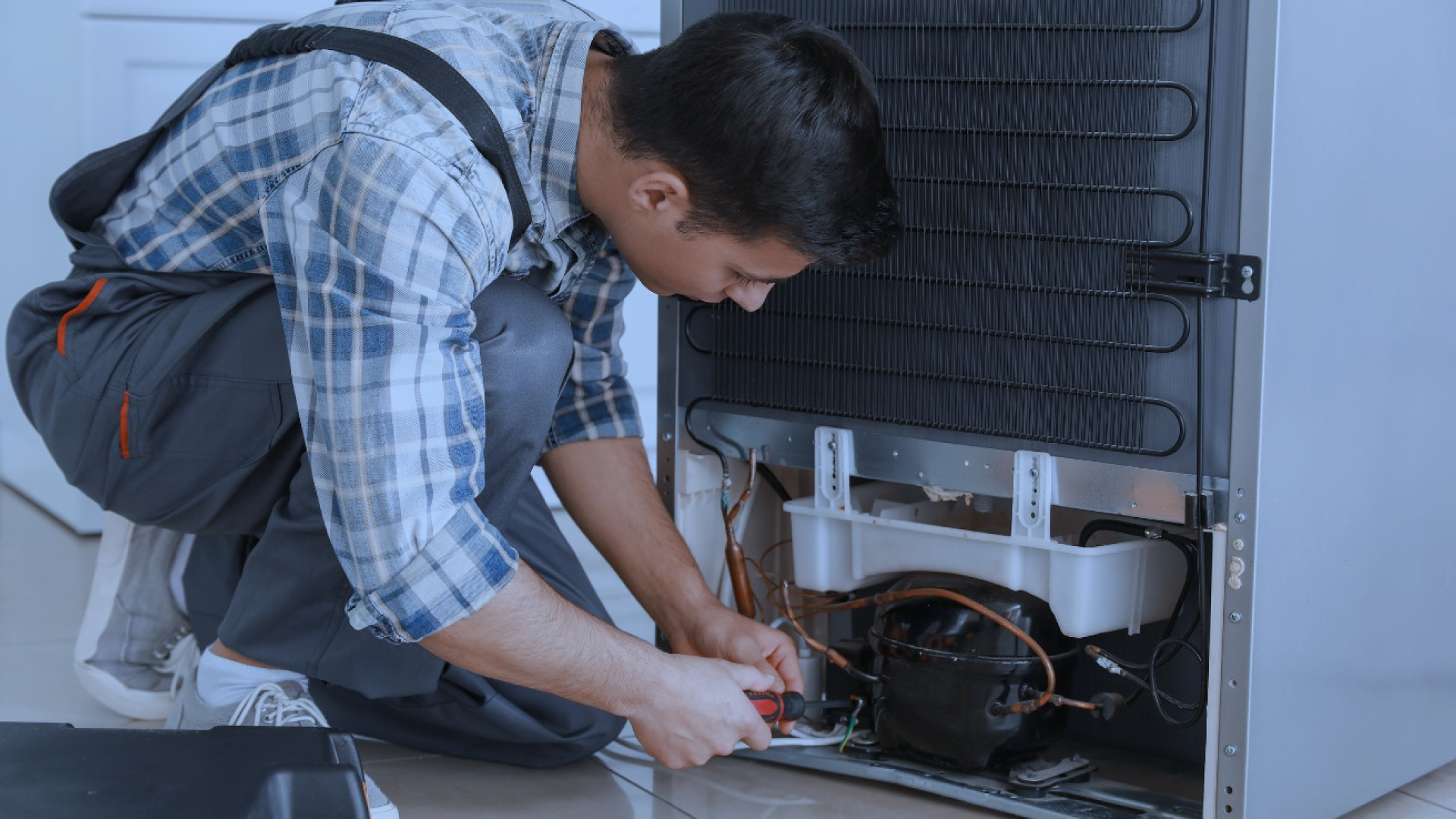 A skilled engineer kneeling and repairing a commercial fridge, performing routine maintenance to ensure optimal cooling performance and energy efficiency.